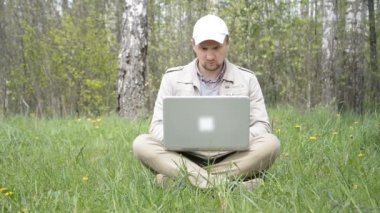 Ön cephede, ormanda dizüstü bilgisayarla çalışan beyaz bir adam.
