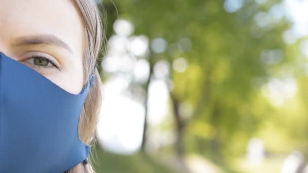 Primer plano de media cara de mujer joven caucásica disgustada en máscara médica azul mirando directamente a la cámara al aire libre — Vídeos de Stock