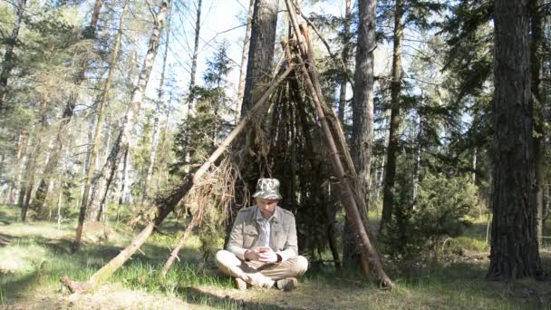 Um homem caucasiano senta-se em uma cabana na floresta e escreve sms em seu telefone, resgatando de uma pandemia no conceito de floresta — Vídeo de Stock