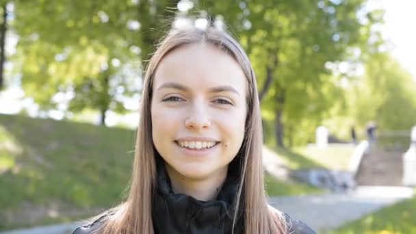 Niedliche junge kaukasische Mädchen Porträt auf einem Hintergrund von grünen Bäumen — Stockvideo