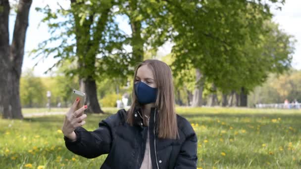 Fiatal nő védő maszkot használ okostelefon videohívás vagy felvétel videó a városi parkban — Stock videók