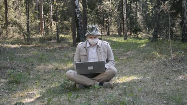 Empresario en máscara está trabajando en portátil en el bosque — Vídeo de stock