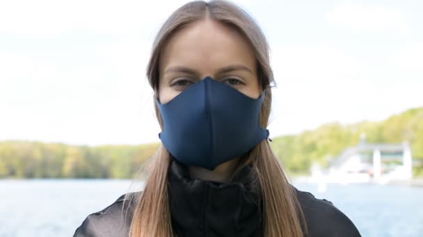 Chica joven con una máscara protectora mirando a la cámara — Vídeos de Stock