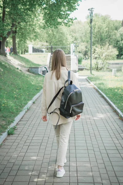 バックパック付きの美しい女子学生が公園の裏側の歩道を歩き — ストック写真