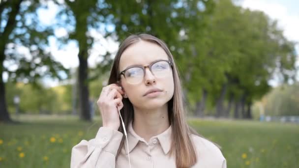 Młoda dziewczyna w słuchawkach słucha muzyki w parku miejskim — Wideo stockowe