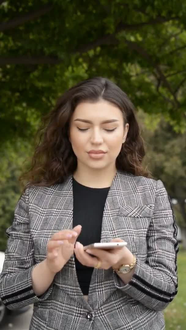 Mujer de negocios en una chaqueta se para y escribe un mensaje por teléfono — Vídeo de stock