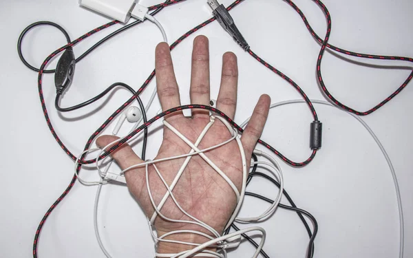 Hand in cords from headphones and chargers, top view on a white background.