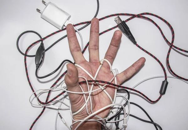 Hand in cords from headphones and chargers, top view on a white background.