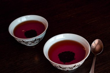 Koyu bir zemin üzerinde siyah çay olan iki seramik kase, bir çay kaşığı, bir çay töreni, minimalizm tarzı..