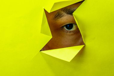 Sarı arka planda yırtık kağıt duvarın içinden geçen tanınmamış bir adamın görüntüsü. Vücut dili kavramı. Duvardaki delik. Bir jest gibi