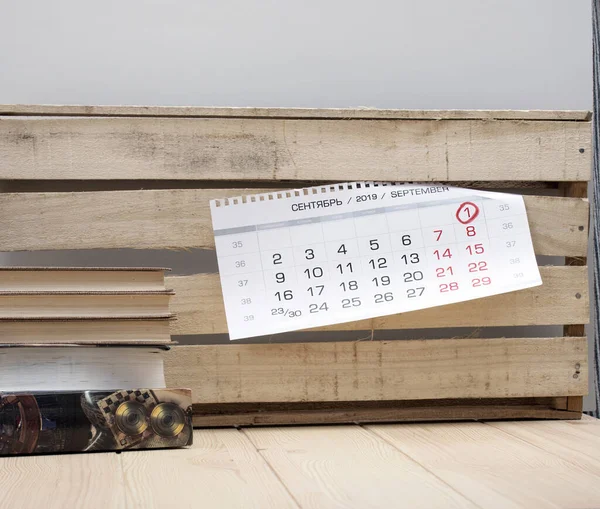 Day of knowledge. Day of the teacher. September the first. Books on a table in light textured wood and a wall calendar with a number highlighted in red marker  one.