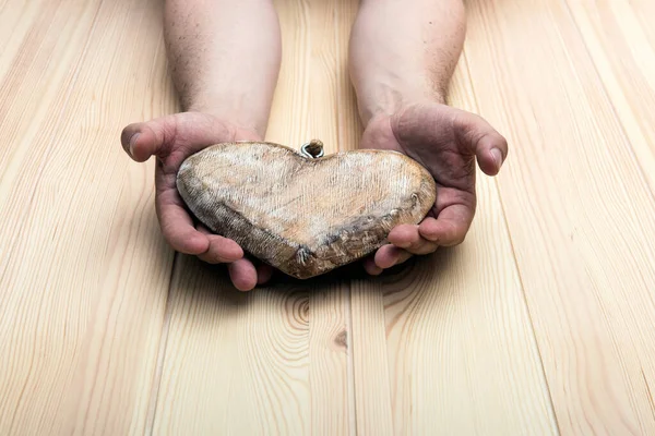 Heart made of wood. Men\'s hands hold a heart on a background of light textured wood.