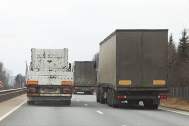 Long vehicle semi trucks traffic, overtaking on a two-lane asphalted highway at spring day, rear view clipart