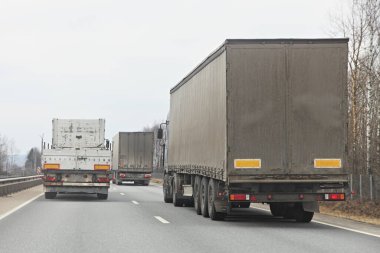 Long vehicle semi trucks overtaking moving on a two-lane asphalted country road at spring day, rear view clipart