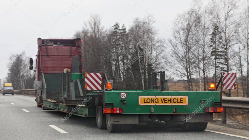 Semi truck with empty green low-frame semi-trailer trawl on suburban asphalted road at spring day, close up rear-side view  Logistics, transportation, trucking industry