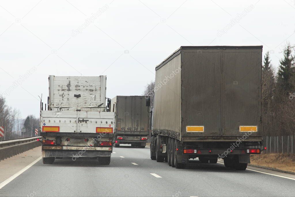 Long vehicle semi trucks traffic, overtaking on a two-lane asphalted highway at spring day, rear view