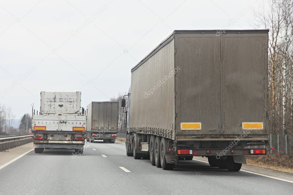Long vehicle semi trucks overtaking moving on a two-lane asphalted country road at spring day, rear view