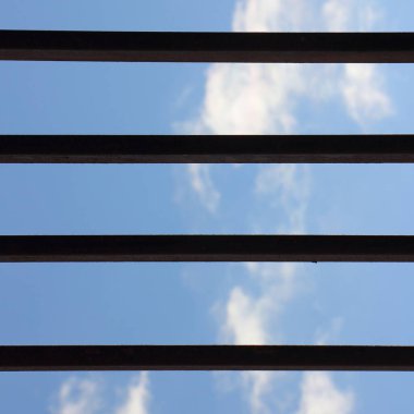 Bulutlu mavi gökyüzü, rendelenmiş yatay demir çubuklardan görüş - kendinden izolasyon kavramı mesaj, karantina, evden uzak çalışma