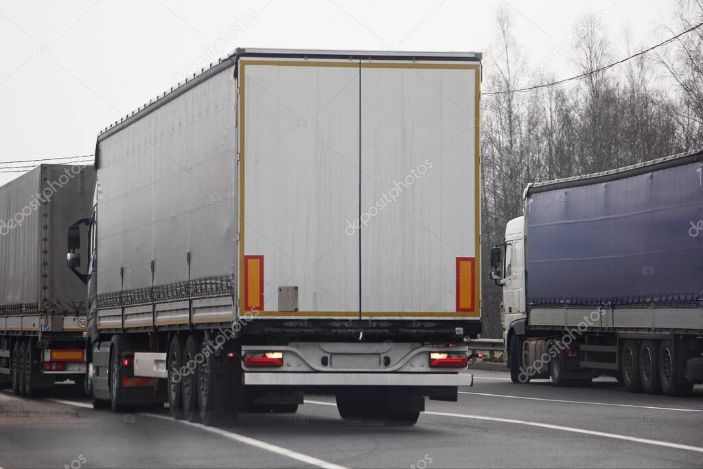 A lot van trucks queue on asphalt road near control point rear view at spring day, transit cargo shipping