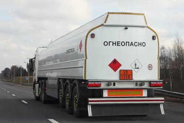 33 1203 tehlikeli sınıf işareti ve Rus alfabesinde yazılı beyaz tırlı yakıt tankeri bir bahar günü banliyö asfalt otoyolunda ilerliyor, dikiz manzaralı ADR özel nakliye kargosunda