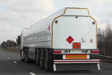 33 1203 tehlikeli sınıf işareti taşıyan beyaz yeni yarı kamyon yakıt tankeri bir bahar günü asfalt yolda ağaçlar ve mavi gökyüzü arka planında, yan manzara ADR tehlikeli kargo, logonuz için yer