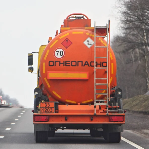 Fuel truck with new bright orange barrel with 33 1203 dangerous class sign and Russian inscription FLAMMABLE move on highway road at spring day, rear view - ADR hazardous gasoline cargo in Russia