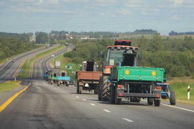 Flatbed karavanlı traktörler asfalt banliyö otobanında güneşli bir yaz gününde gezerler, tarımsal mekanizasyon, perspektifte arka manzara