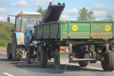 Düz karavanlı traktör, güneşli bir yaz gününde kır yolunda gezintiye çıkıyor. Tarımsal mekanizasyon, perspektif olarak arka taraf manzarası.