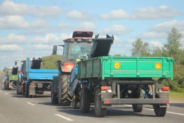 Düz karavanlı traktörler, güneşli bir yaz gününde kır yolunda gezerler, tarımsal mekanizasyon, perspektifte arka taraf manzarası