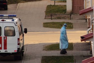 Antiviral mavi üniformalı bir doktor ambulans arabasından eski bir eve gider.