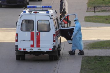 Mavi elbiseli, ayakkabılı, tıbbi maskeli ve eldivenli bir doktor ambulans arabasına gidiyor.
