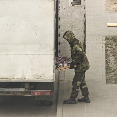 Kamuflaj kıyafetli, kapüşonlu bir adam kamyondan ekmek indiriyor.