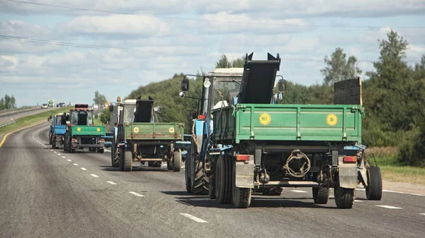 晴れた夏の日に郊外の道路にフラットベッドトレーラー付きの多くのトラクター船団 農業機械化 視点でリアサイドビュー — ストック写真