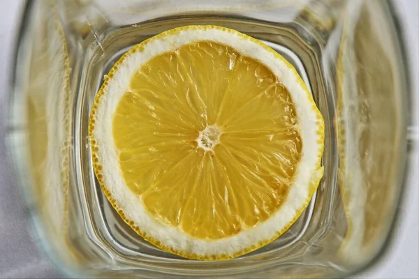 A round slice of juicy lemon at the bottom of a square glass