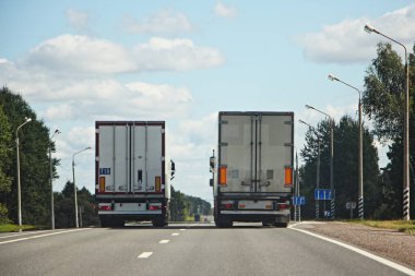 Two parallel course semi trucks on summer road on trees and streetlightl on roadsides and blue sky with clouds background clipart