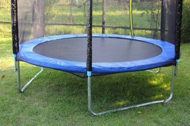 Modern empty 8ft trampoline with outside pritection net on green grass on a summer day close-up, fitness outdoor training clipart