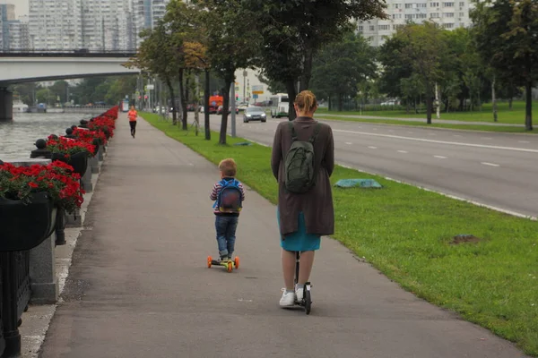 夏日傍晚 在大城市的户外度假 一个女人和一个男孩骑着踢踏车在公园的一条路上 — 图库照片
