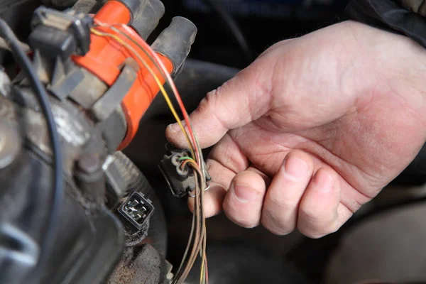 汽车发动机诊断时 机械师的手将连接器从冷却剂温度传感器上取出 作为点火分配器的背景 — 图库照片