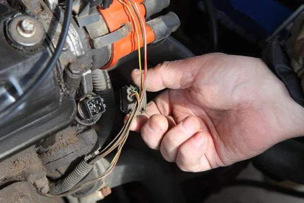 Old car gasoline engine motor repair, mechanic's hand connect the connector socket on the antifreeze temperature sensor on the background of the ignition distributor