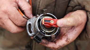 Kapağı olmayan parçalanmış araba ateşleme dağıtıcısı ve servis elemanlarının elinde dirençli kamera, benzinli motor ateşleme sistemi bakımı.