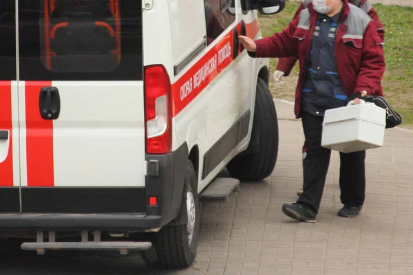 白いスーツケースとロシア語の碑文Ambulanceと医療用マスクオープン救急車の車で赤い服の医者 人々の抗ウイルス予防 — ストック写真