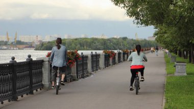 At kuyruklu ince bir adam ve kasksız küçük bir kadın yaz günü yol kenarında bisiklet sürerler, arkadan manzara, açık hava tatili.