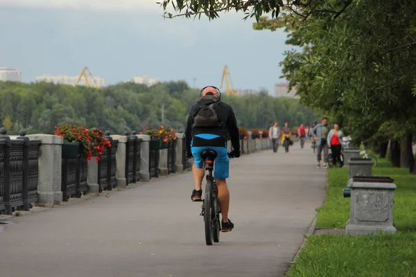 一个骑自行车的人 穿着运动服 头戴耳机 背着背包 骑着自行车在夏天的傍晚沿着人行道上 后视镜 — 图库照片