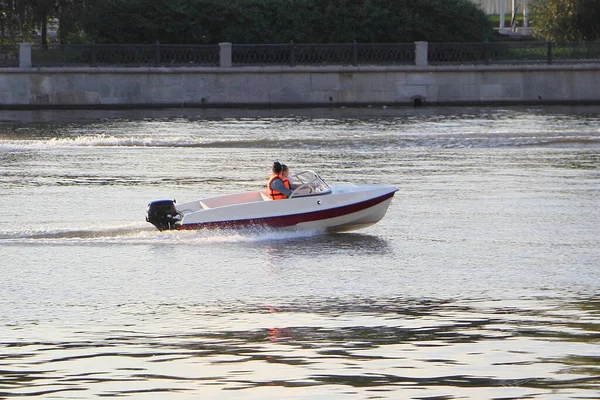 夏の日に都市堤防の背景に川に浮かぶライフジャケットに2人の乗客を持つ1つの非登録9 9馬力のプラスチック製の船 — ストック写真