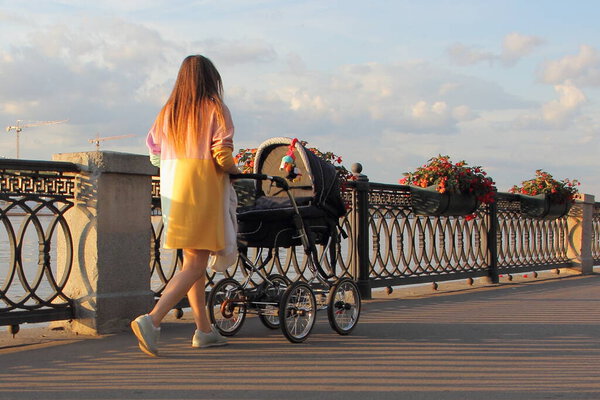 A young mother woman in a dress walks with a baby stroller in a Park on a Sunny summer day, maternal care
