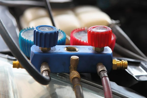 Car A/C testing equipment close up, red and blue valves with manometers and pipes under the hood of the car, vehicle air conditioner repair service and maintenance