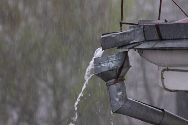 Çatıdan gelen yağmur suyu, eski su birikintisinin bacasından taşar. Kentte şiddetli bir yağmur fırtınası var.