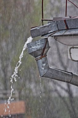 A stream of rainwater from the roof overflows through the funnel of the drain close-up, a heavy downpour in the city clipart