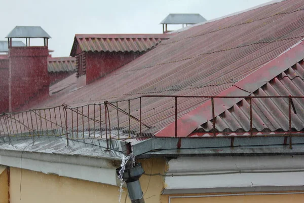 A rain water from the red roof overflows through the funnel of the gutter, a heavy rainstorm in the European city