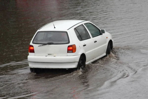 白い車の道路上の波と大きな水たまりを介して大雨 地元の洪水 リア側のビュー中に運転している — ストック写真